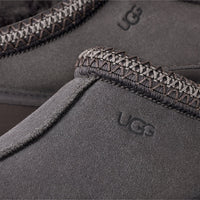 Close-up of UGG branded gray slippers with textured trim on a light gray background
